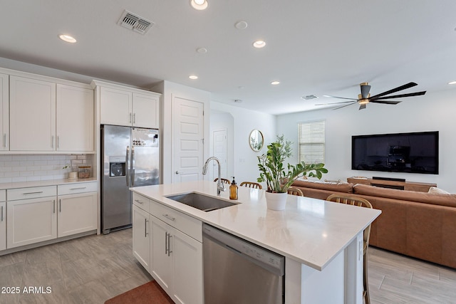 kitchen featuring stainless steel appliances, a sink, visible vents, white cabinets, and backsplash