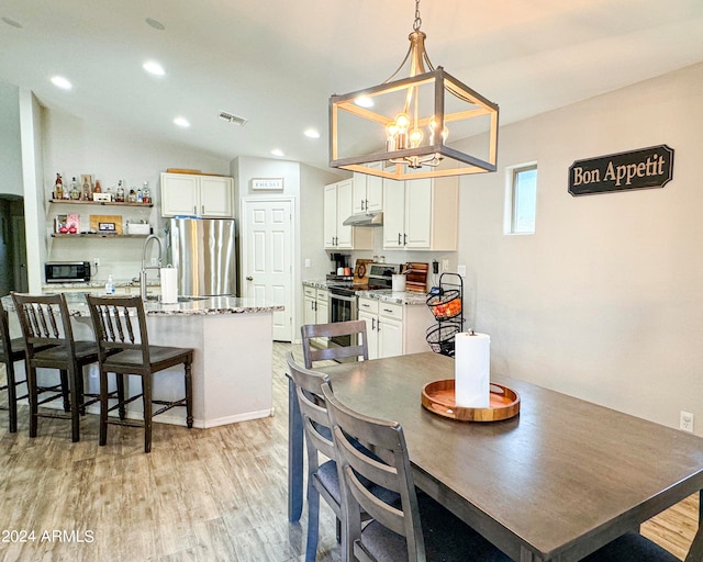 dining area with light hardwood / wood-style floors, lofted ceiling, and an inviting chandelier