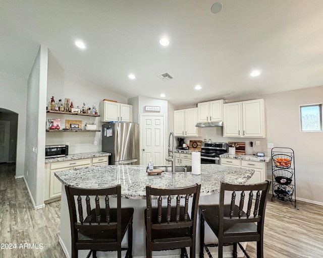 kitchen featuring light hardwood / wood-style flooring, appliances with stainless steel finishes, an island with sink, lofted ceiling, and a breakfast bar