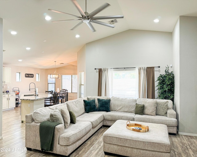 living room with sink, light hardwood / wood-style floors, lofted ceiling, and ceiling fan with notable chandelier