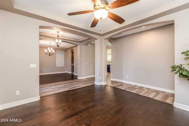 spare room with ceiling fan with notable chandelier, dark hardwood / wood-style flooring, and a tray ceiling