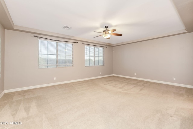 carpeted empty room with a raised ceiling and ceiling fan