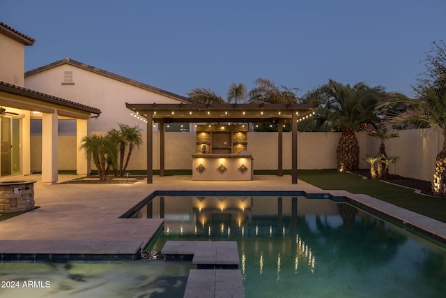 pool at dusk featuring a patio area and an outdoor kitchen