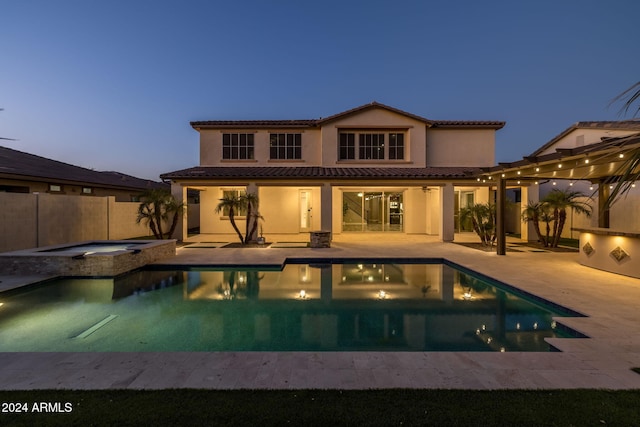 pool at dusk with an in ground hot tub and a patio area