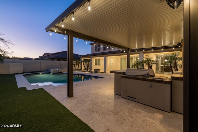 pool at dusk with area for grilling, a patio area, and exterior kitchen