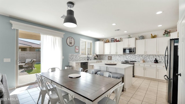 kitchen featuring white cabinets, appliances with stainless steel finishes, decorative light fixtures, and a healthy amount of sunlight