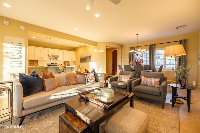 tiled living room with ceiling fan with notable chandelier