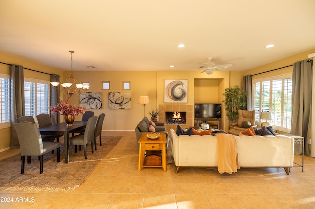 tiled living room with ceiling fan with notable chandelier and a fireplace