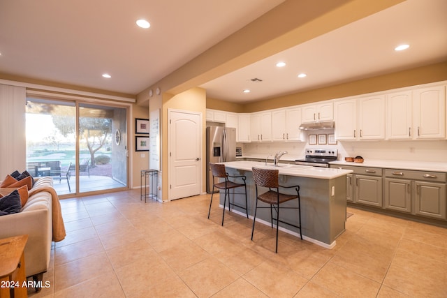 kitchen with a breakfast bar area, stainless steel appliances, a center island with sink, light tile patterned floors, and white cabinets