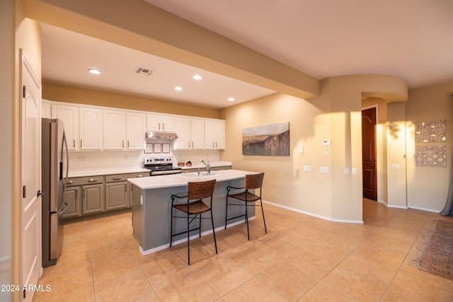 kitchen with stainless steel appliances, a center island with sink, a breakfast bar, light tile patterned flooring, and white cabinets