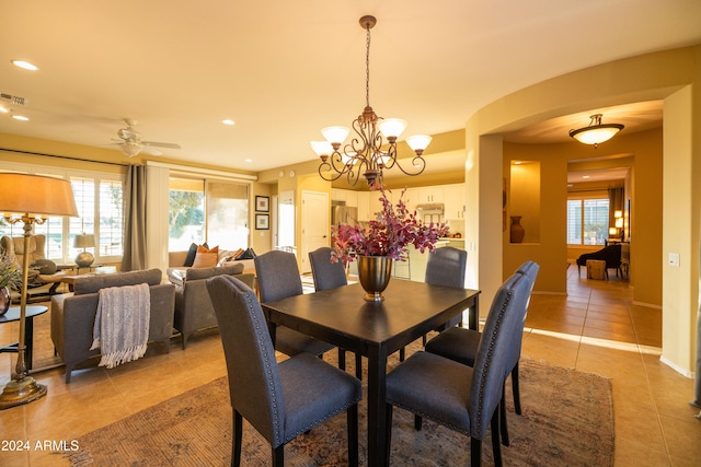 tiled dining area with ceiling fan with notable chandelier and a healthy amount of sunlight