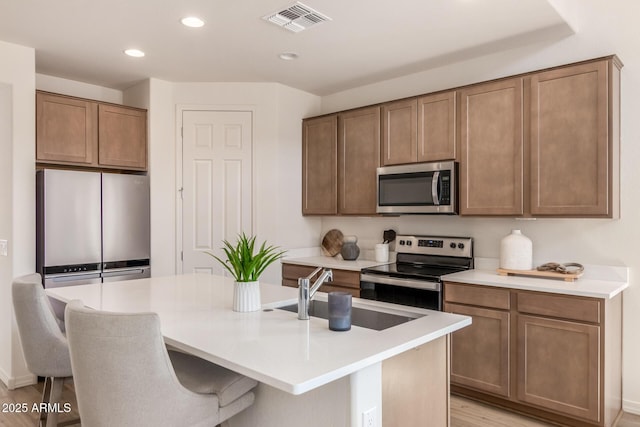 kitchen with a kitchen island with sink, a kitchen breakfast bar, sink, appliances with stainless steel finishes, and light hardwood / wood-style floors