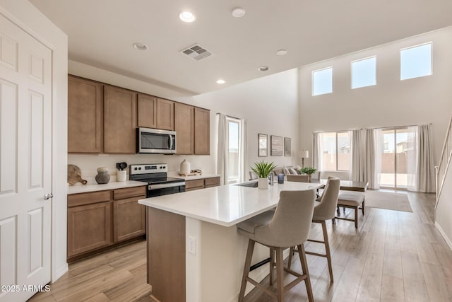 kitchen with appliances with stainless steel finishes, an island with sink, a kitchen bar, a high ceiling, and light hardwood / wood-style floors