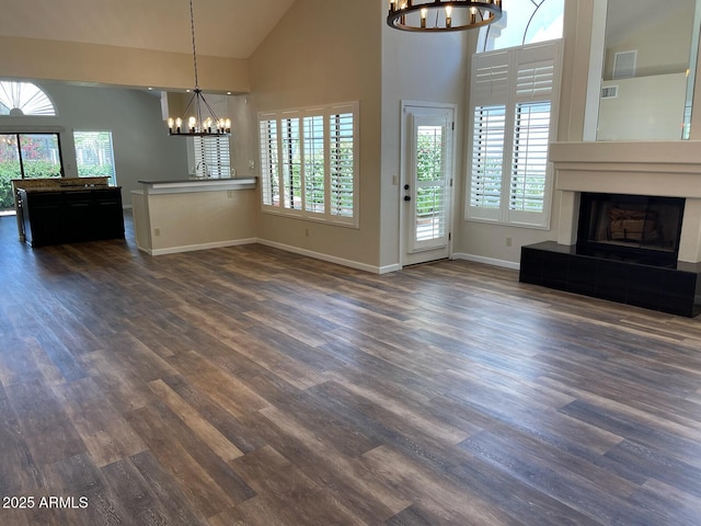 unfurnished living room with a fireplace with raised hearth, high vaulted ceiling, an inviting chandelier, and dark wood-type flooring