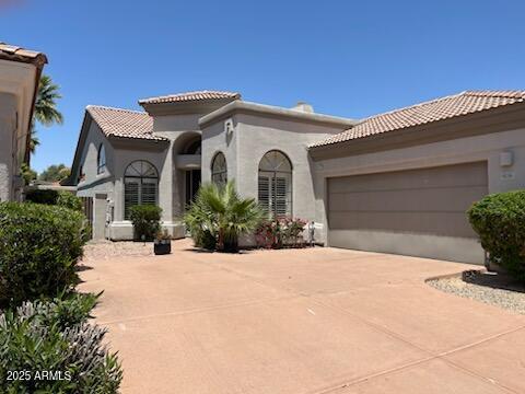 mediterranean / spanish home with an attached garage, stucco siding, a tile roof, and concrete driveway