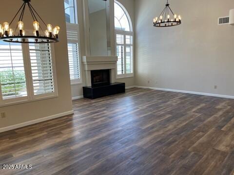 unfurnished living room featuring dark wood-style flooring, visible vents, baseboards, a fireplace with raised hearth, and an inviting chandelier