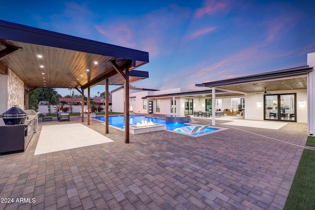 pool at dusk with a patio area, exterior kitchen, and an in ground hot tub