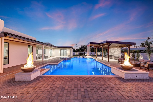 pool at dusk with an outdoor fire pit and a patio