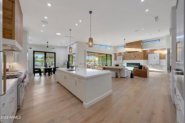 kitchen featuring high end stove, an island with sink, white cabinetry, light hardwood / wood-style flooring, and decorative light fixtures