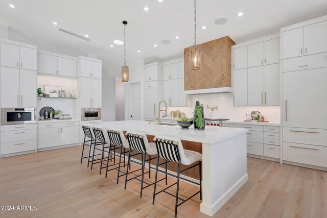 kitchen featuring sink, light wood-type flooring, an island with sink, a kitchen breakfast bar, and white cabinets