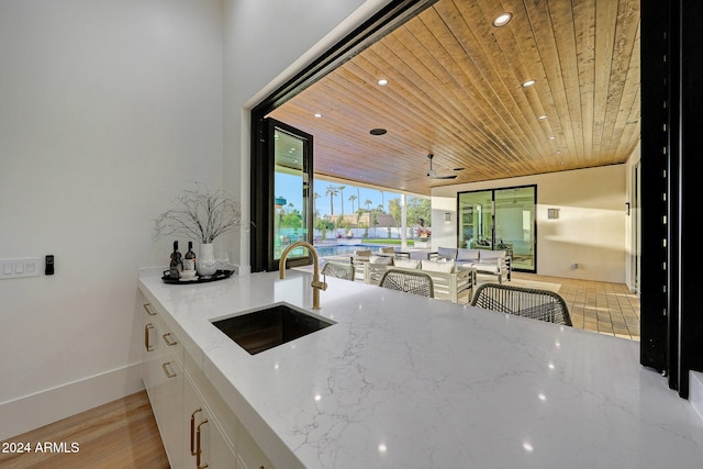 kitchen with sink, light hardwood / wood-style floors, wooden ceiling, white cabinets, and light stone counters