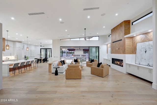 living room featuring high vaulted ceiling, a tiled fireplace, light wood-type flooring, and ceiling fan