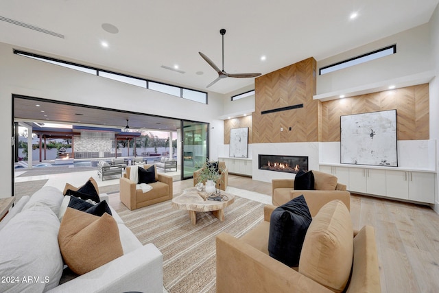 living room featuring ceiling fan, a high ceiling, light wood-type flooring, and a fireplace