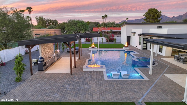 pool at dusk with a bar, a mountain view, pool water feature, a fire pit, and a patio area