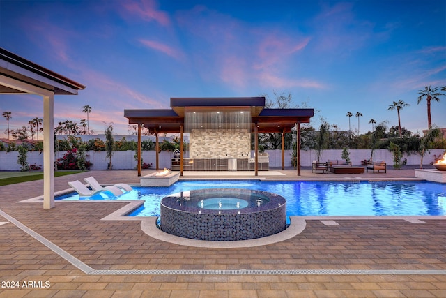 pool at dusk featuring a patio and an in ground hot tub