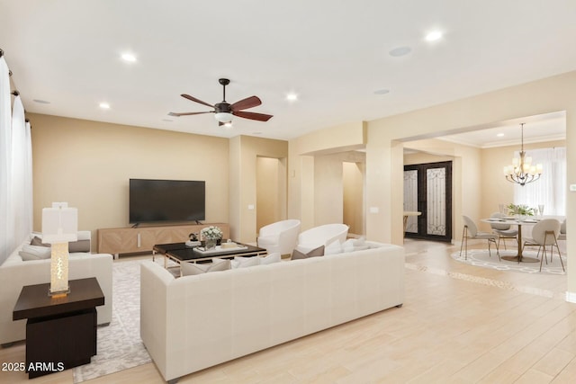 living room with ceiling fan with notable chandelier, light wood-type flooring, and crown molding