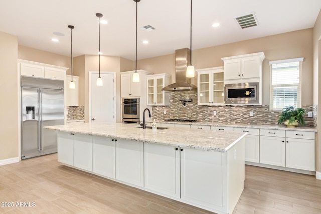 kitchen with a center island with sink, built in appliances, white cabinetry, and range hood