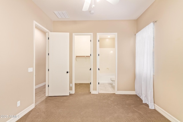 unfurnished bedroom featuring a closet, ceiling fan, a walk in closet, light carpet, and ensuite bathroom