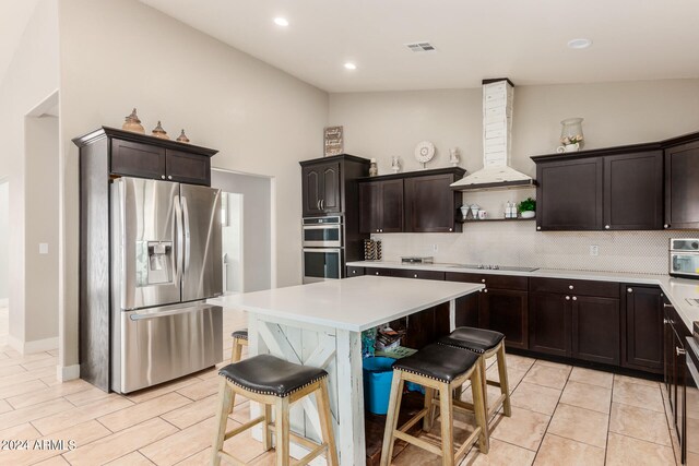 kitchen with appliances with stainless steel finishes, dark brown cabinets, a kitchen breakfast bar, and exhaust hood