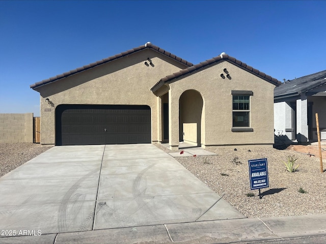 mediterranean / spanish-style house featuring stucco siding, an attached garage, fence, driveway, and a tiled roof