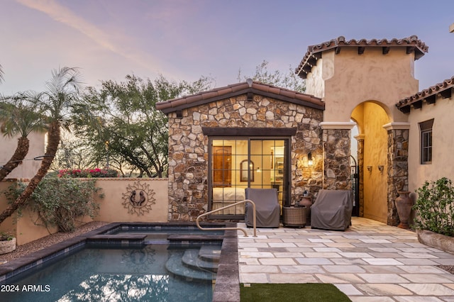 pool at dusk with an in ground hot tub and a patio