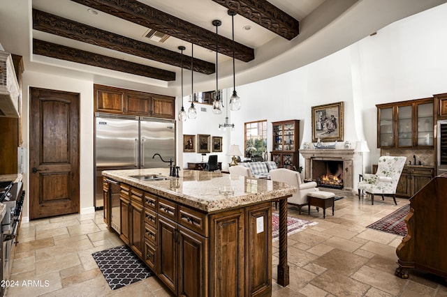 kitchen with sink, hanging light fixtures, light stone countertops, an island with sink, and beam ceiling