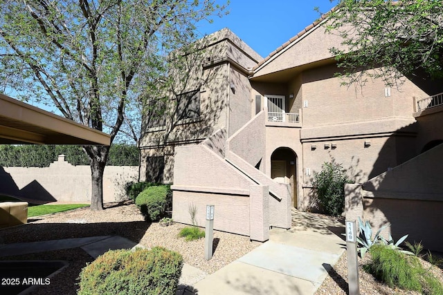 view of home's exterior featuring a balcony, stucco siding, fence, and a tiled roof