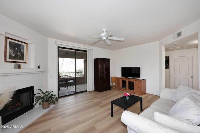 living room featuring a ceiling fan, light wood-type flooring, visible vents, and a tile fireplace