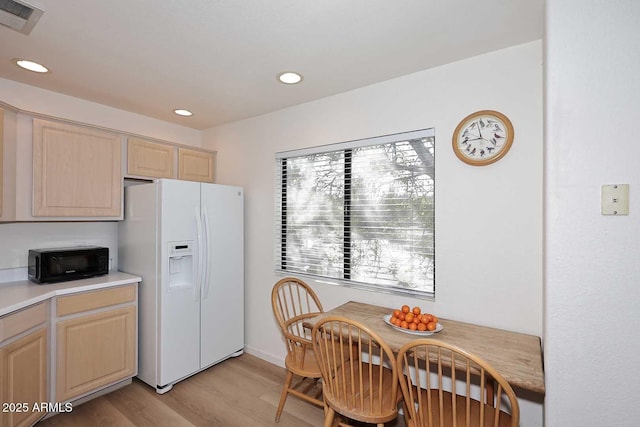 kitchen with white refrigerator with ice dispenser, visible vents, light countertops, light brown cabinets, and black microwave