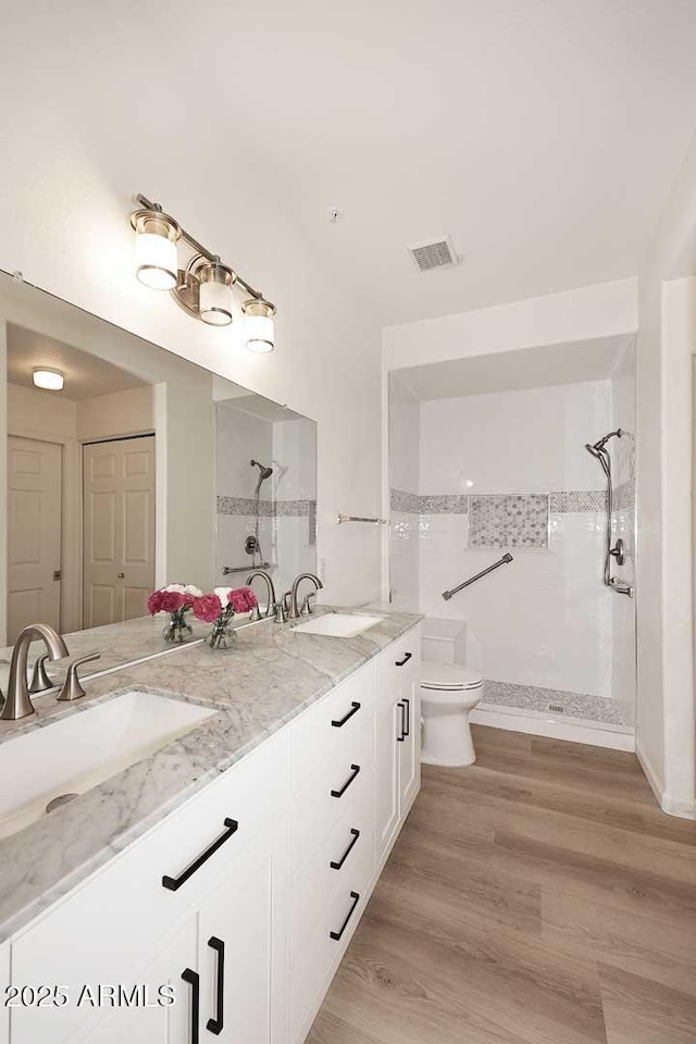 full bathroom featuring double vanity, visible vents, toilet, a sink, and a tile shower