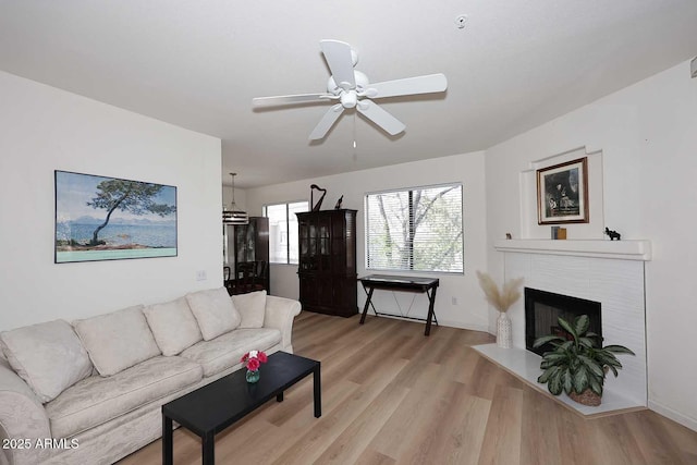 living room featuring a fireplace with flush hearth, a ceiling fan, and light wood-style floors