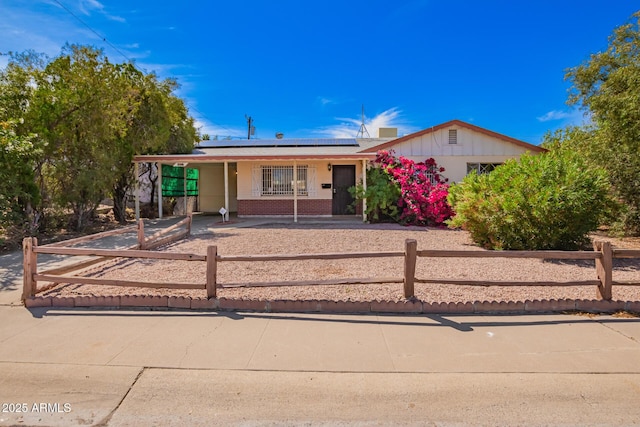 ranch-style home featuring roof mounted solar panels, a fenced front yard, and brick siding