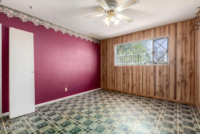 unfurnished room with wood walls, tile patterned floors, baseboards, and a ceiling fan