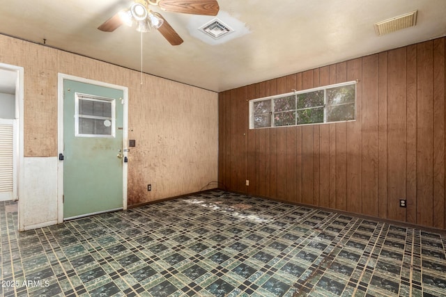 spare room featuring wooden walls, a ceiling fan, and visible vents