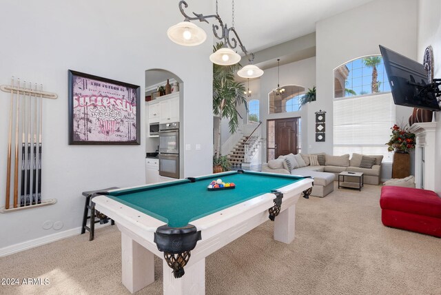 carpeted living room with a high ceiling, a notable chandelier, a premium fireplace, and a healthy amount of sunlight