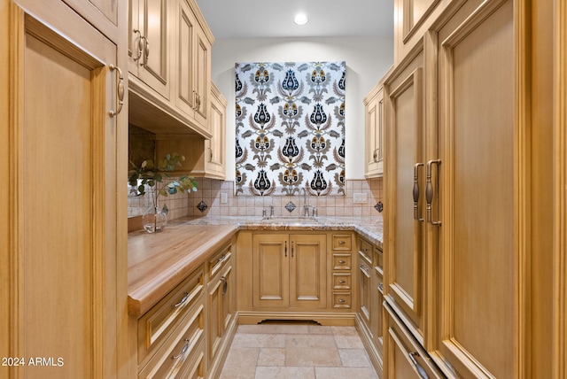 kitchen featuring light tile floors, sink, tasteful backsplash, and light stone counters