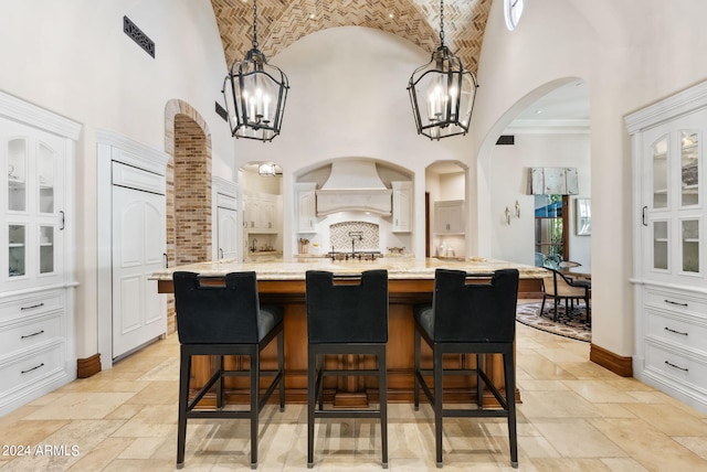 kitchen featuring a towering ceiling, an inviting chandelier, custom exhaust hood, and decorative light fixtures