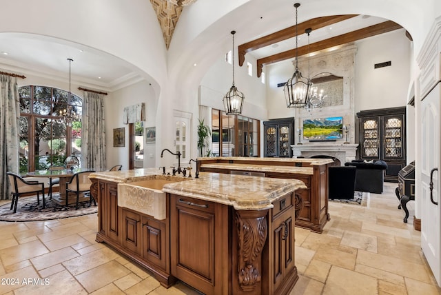 kitchen with an island with sink, an inviting chandelier, light stone counters, a high ceiling, and hanging light fixtures