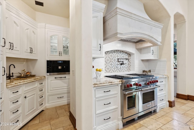 kitchen featuring white cabinetry, range with two ovens, custom range hood, tasteful backsplash, and light tile flooring