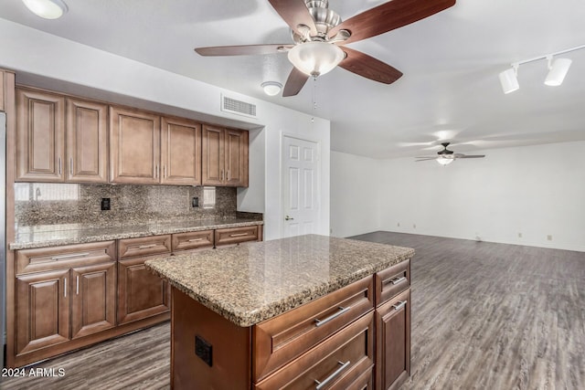 kitchen with rail lighting, dark hardwood / wood-style floors, decorative backsplash, a kitchen island, and light stone counters